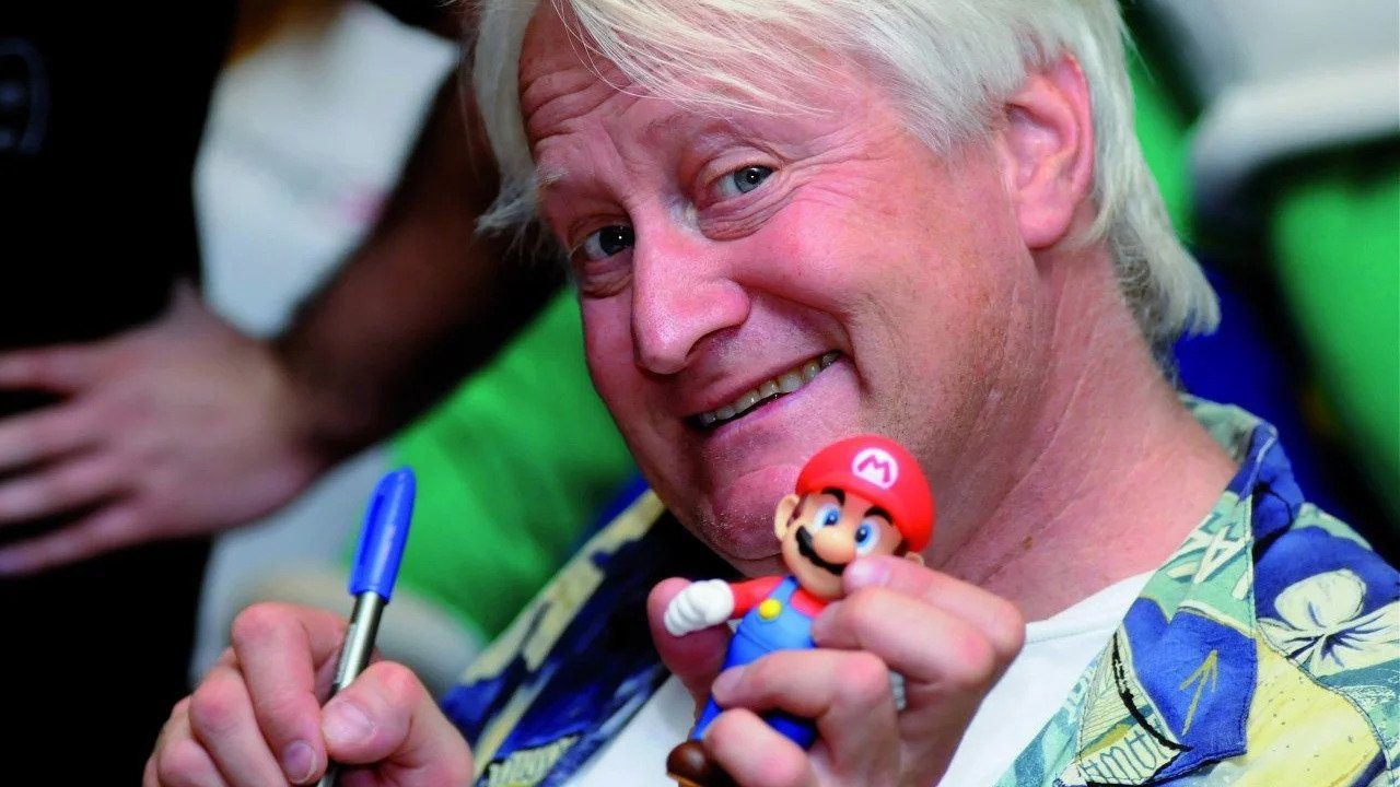 Charles Martinet holding a pen and mario figure, smiling at the camera.